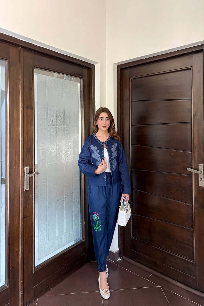 Woman wearing denim jogger pants with embroidery, standing by wooden doors.